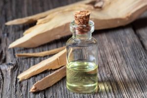 A bottle of sandalwood essential oil with white sandalwood on a table