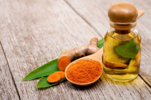 Turmeric essential oil and tumeric powder with green leaf isolated on wood table background.