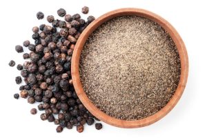 Ground black pepper in a wooden bowl and peppercorns close-up on a white background, isolated. Top view